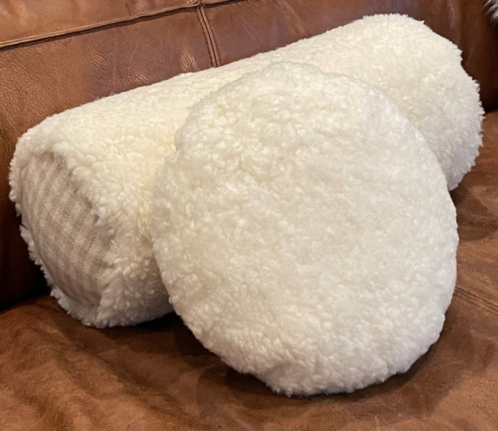 natural white shearling fur pillows in bolster style and round styled on brown leather couch
