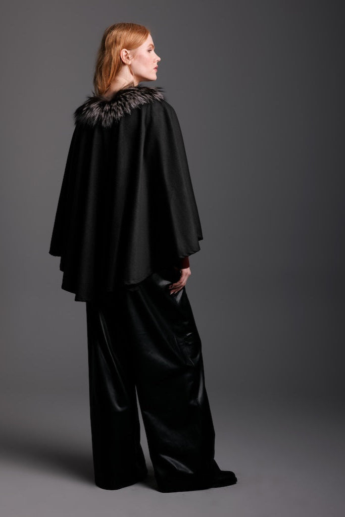 woman wearing black cashmere cape with silver fox trim  black leather pants back detail view