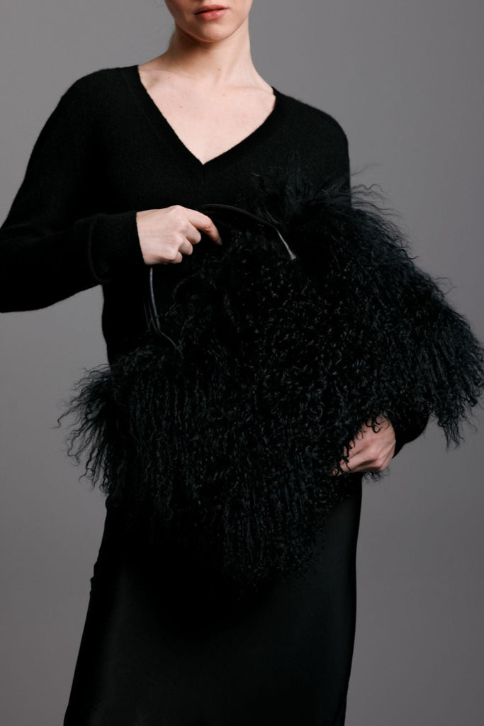 woman wearing a black dress holding a black mongolian lamb fur handbag with leather handles
