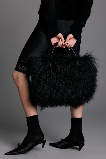 black mongolian lamb handbag with leather handles and interior pockets worn on model with silk skirt