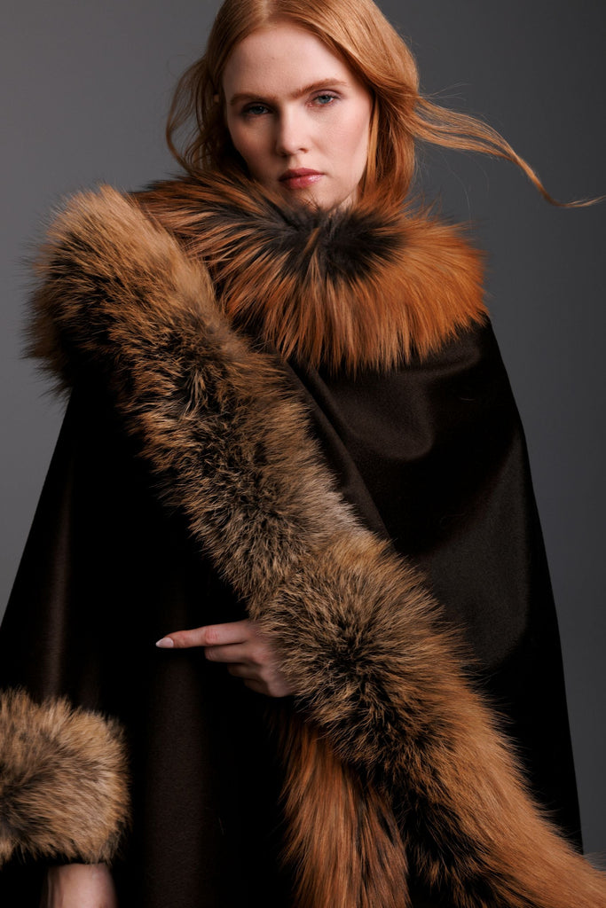 Woman wearing a brown cashmere cape with gold fox fur trim all around close up