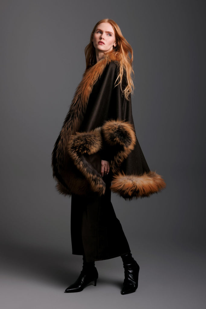 Woman wearing a brown cashmere cape with gold cross fox trim all around and a black skirt and black boots