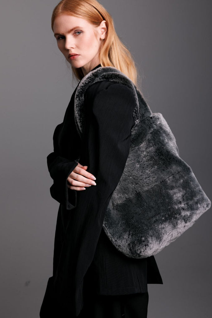 woman wearing black suit and accessorised with  a grey real fur shearling tote bag