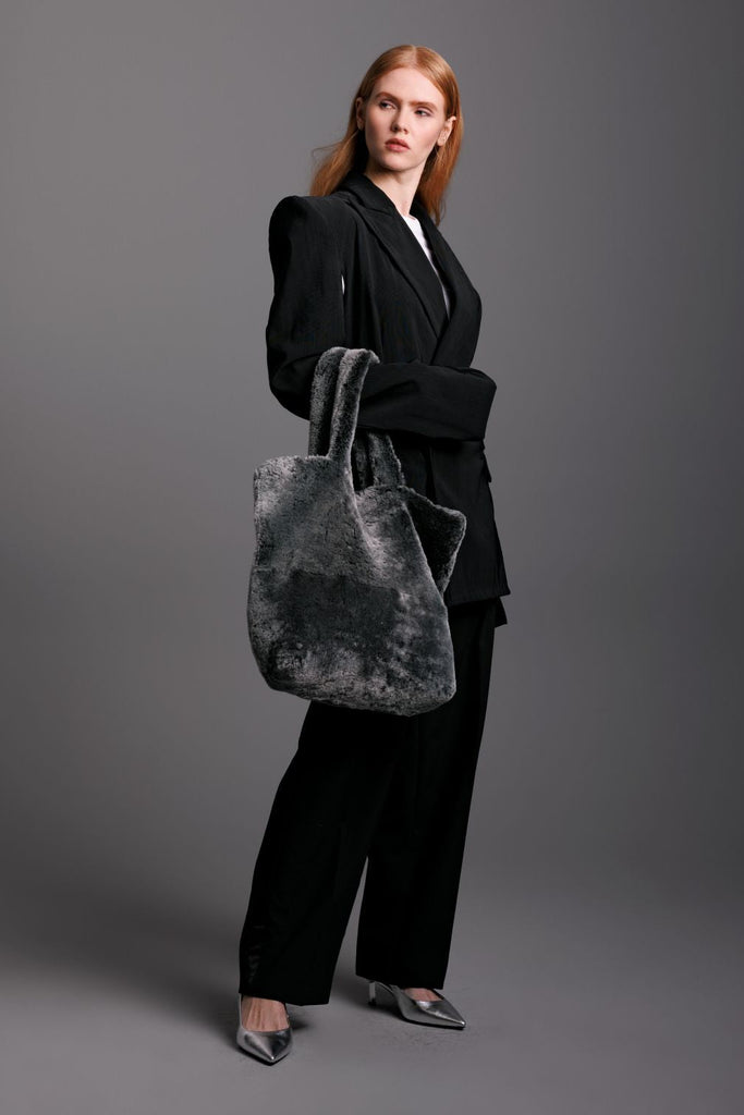 woman wearing a grey shearling tote bag over her arm with a black suit and silver heels 