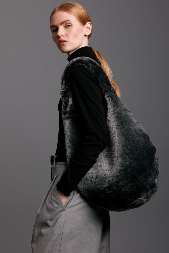 woman holding a grey shearling hobo bag over her shoulder with grey pants on