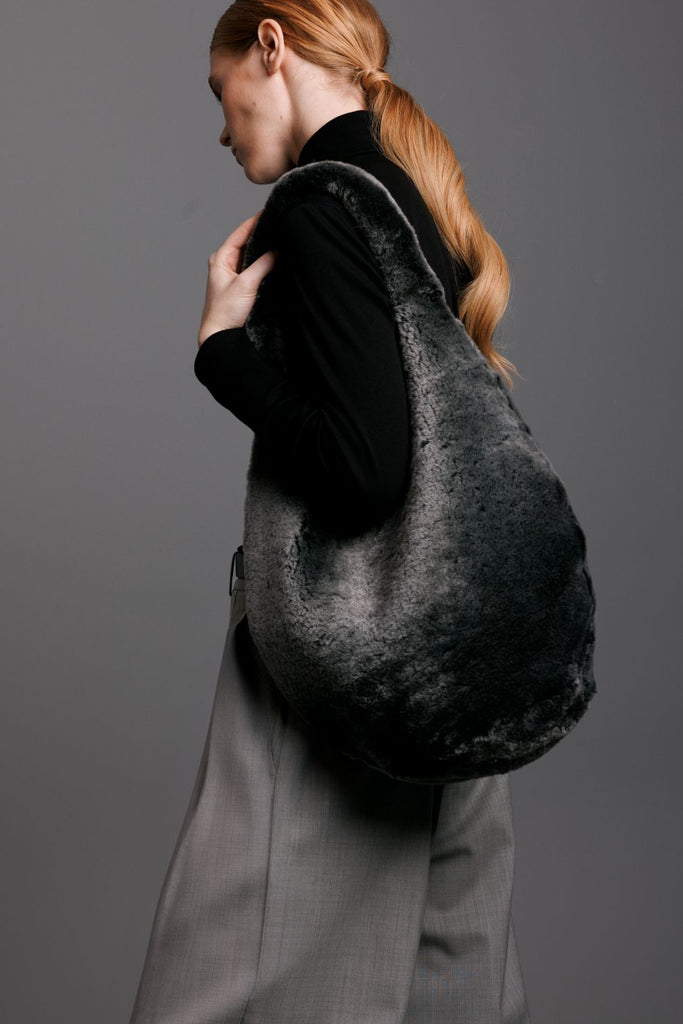 woman wearing a grey shearling hobo bag with shearling interior and grey pants black sweater