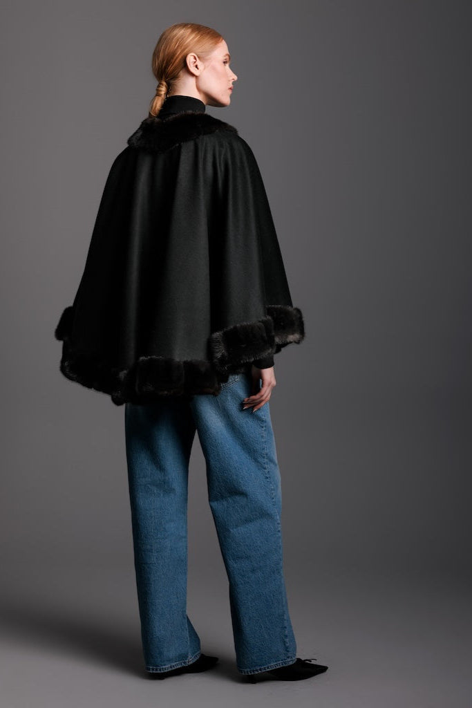 woman wearing black cape with mink cashmere trim and denim and heels with detail view of the back.