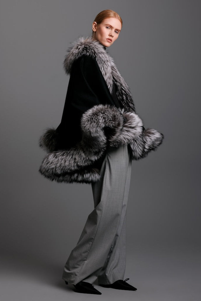 woman wearing black cashmere silver fox fur trim cape with grey pants and heels with a detail view from the side