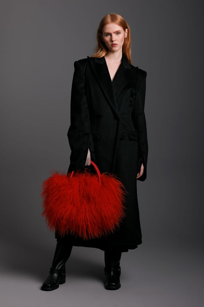 Woman in a black coat holding a red fluffy mongolian lamb bag with red leather straps and black boots