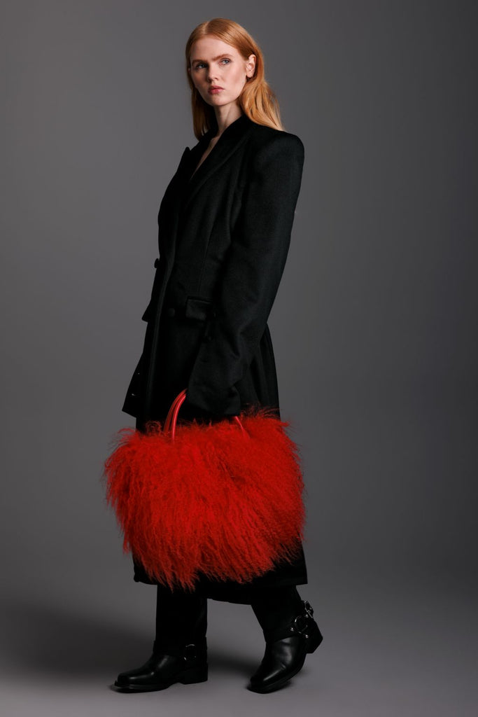 Woman holding a red mongolian lamb handbag with boots on and black cashmere coat