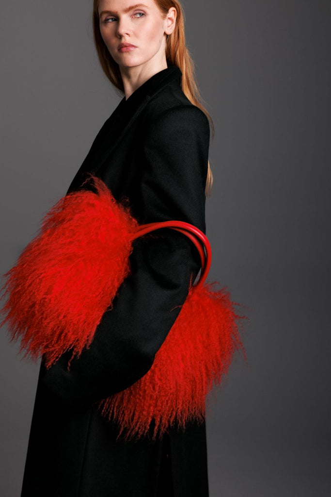 Woman wearing a black cashmere coat holding a read mongolian lamb handbag with red handles